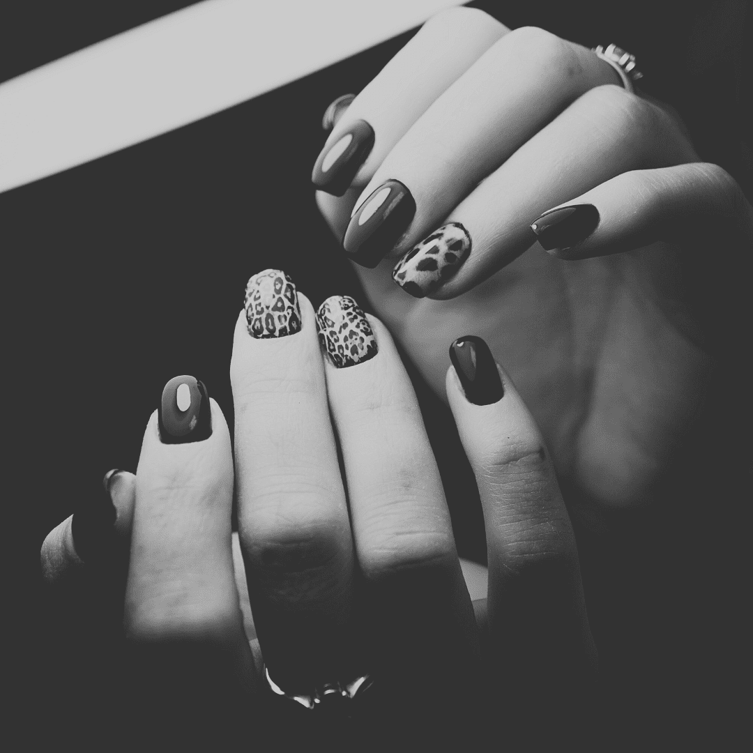 Black and white photo of hands with leopard print and solid dark nail designs.