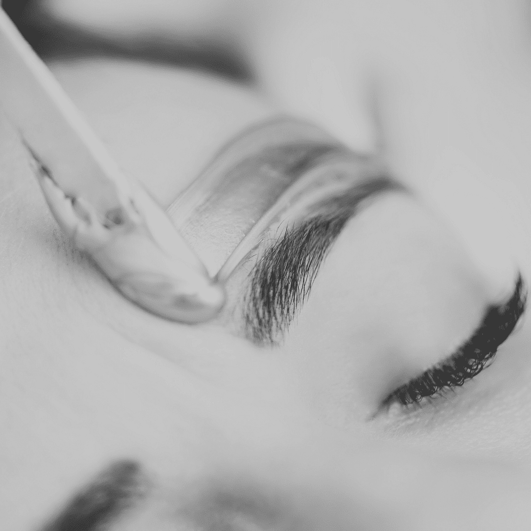 Close-up of a person receiving an eyebrow treatment, applying brush strokes to shape brows.